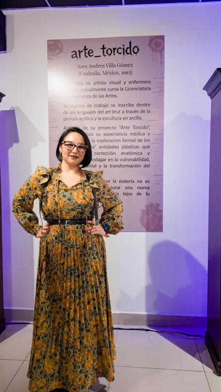 Sara Villa, de vestido largo estampado, frente al panel de sala con su semblanza