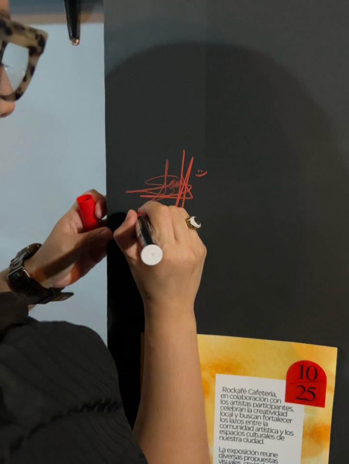 Sara Villa escribe con marcador rojo sobre la pared negra del café, junto a su cuadro